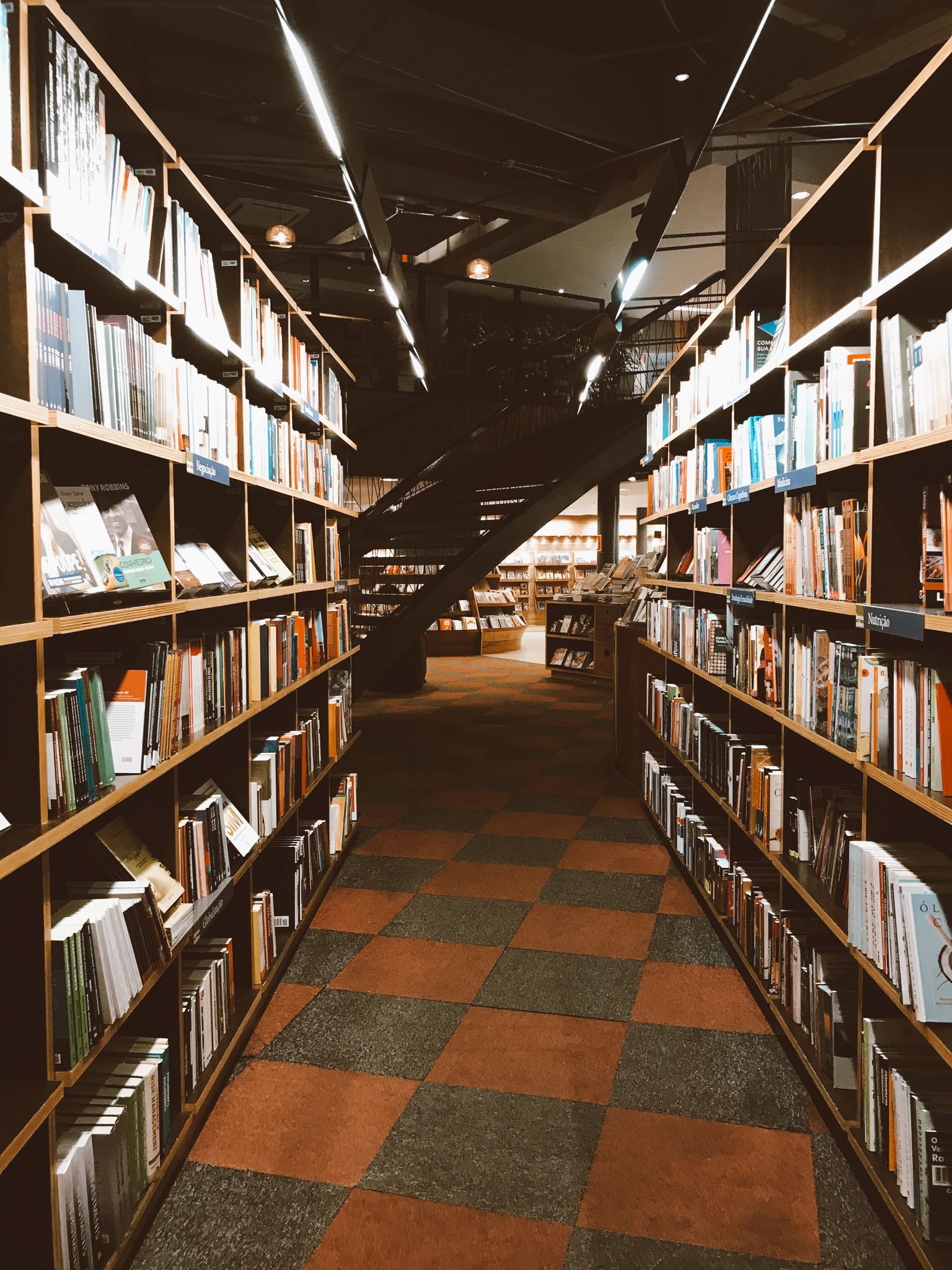 Warmly lit library aisle filled with a vast collection of books on wooden shelves.